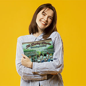 young woman holding the daring diaries book to her chest in front of a yellow background