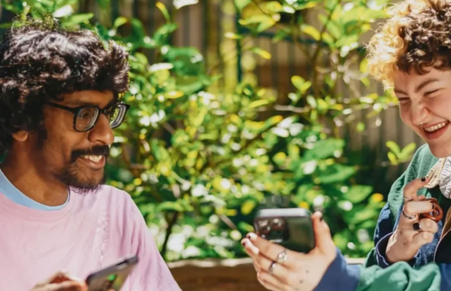 Two friends with and without visual disabilities holding their smartphones and laughing