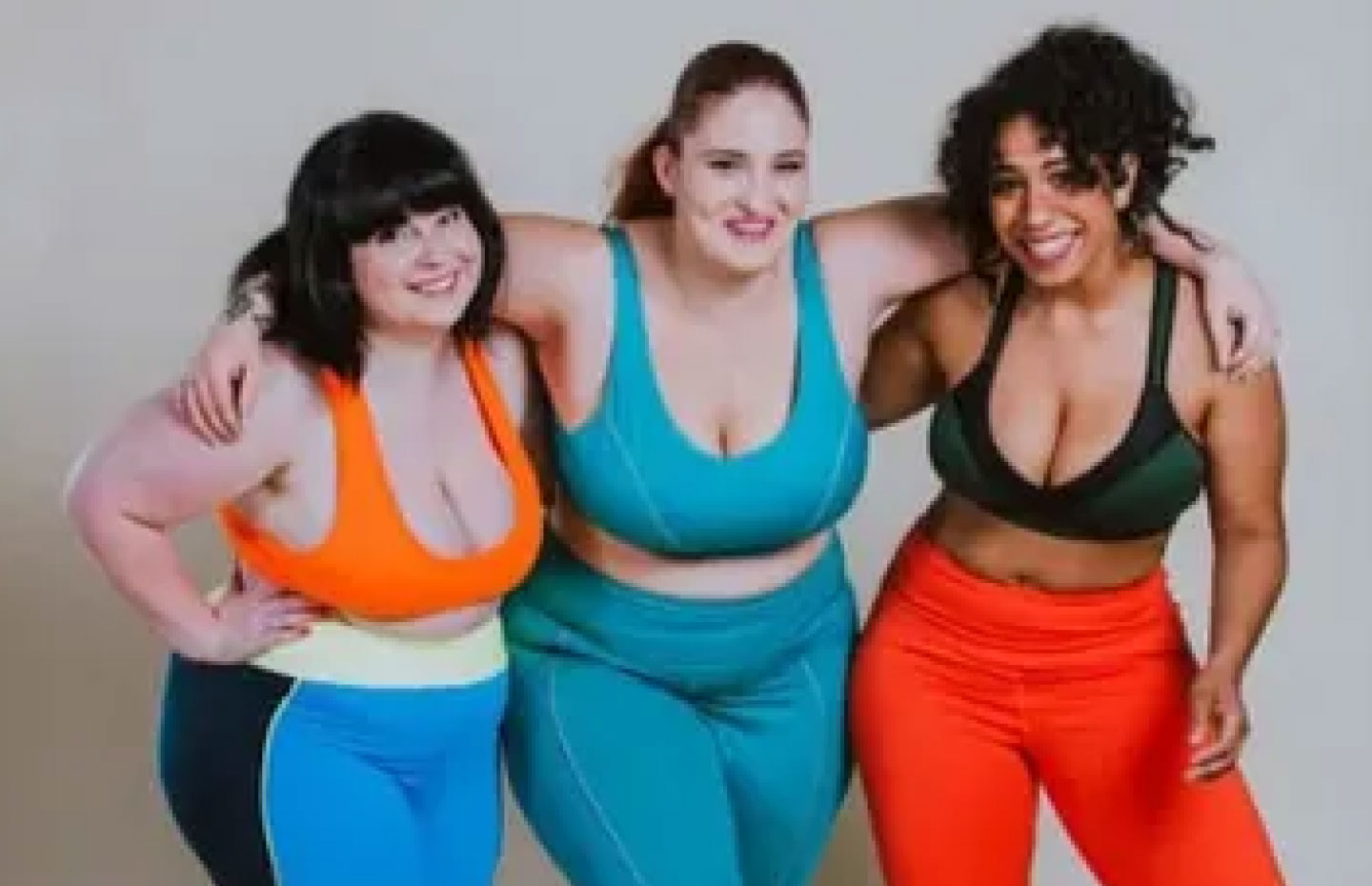 3 women with and without visual disabilities in workout clothing smiling with their arms around each other