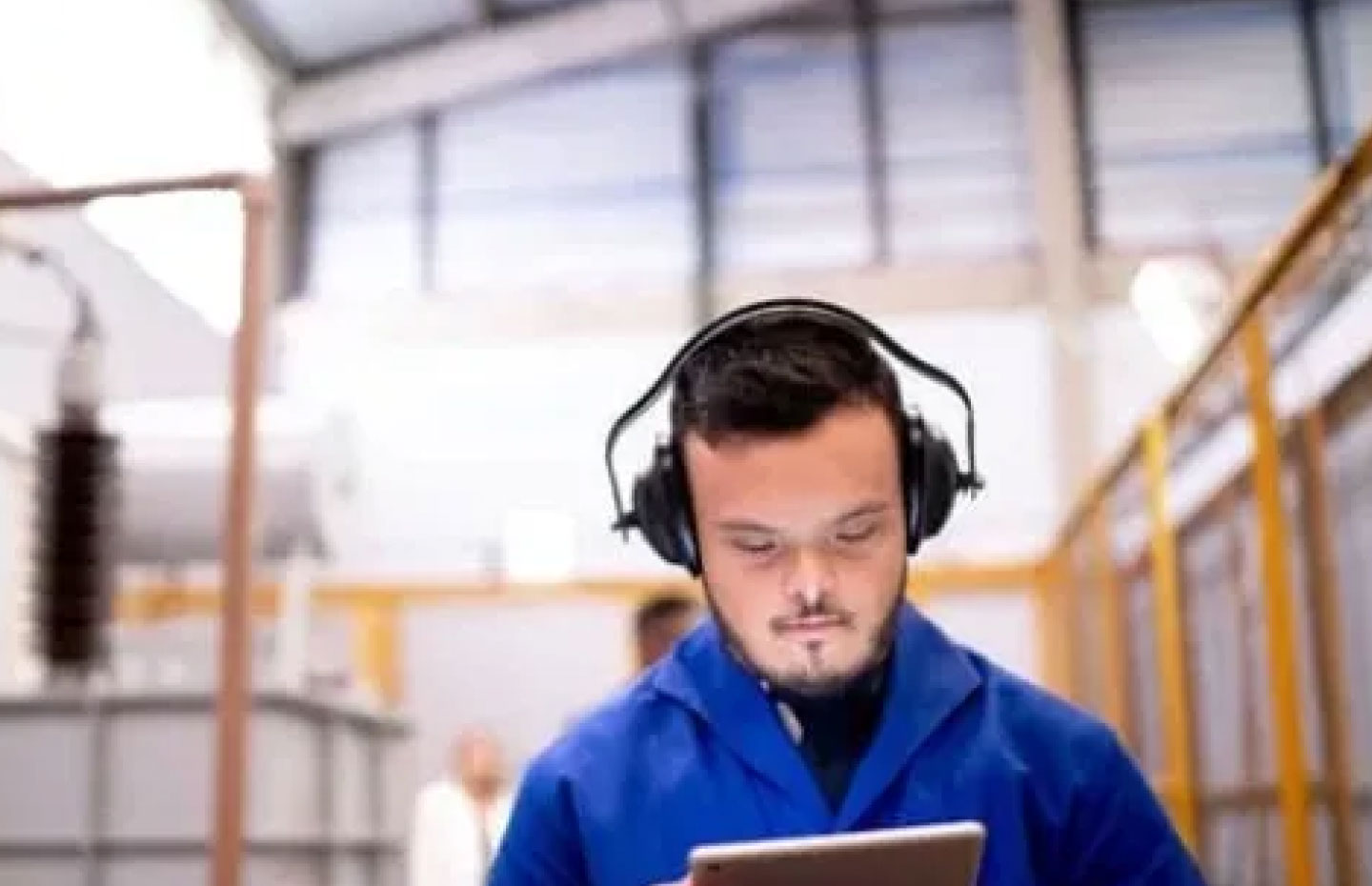 Man with down syndrome at work in a warehouse looking at a tablet with headphones