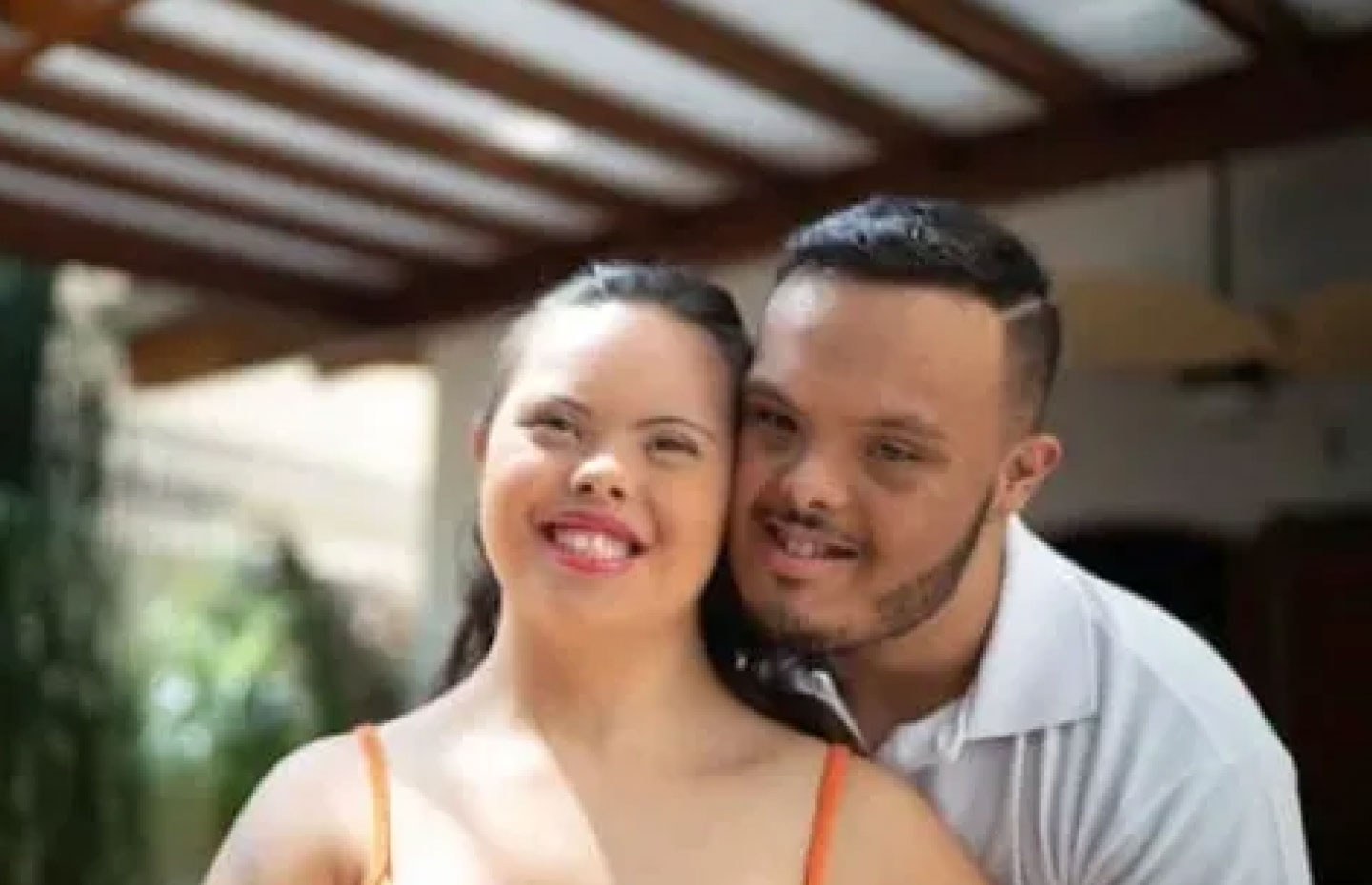 A man with down syndrome embracing a woman with down syndrome from behind her outside