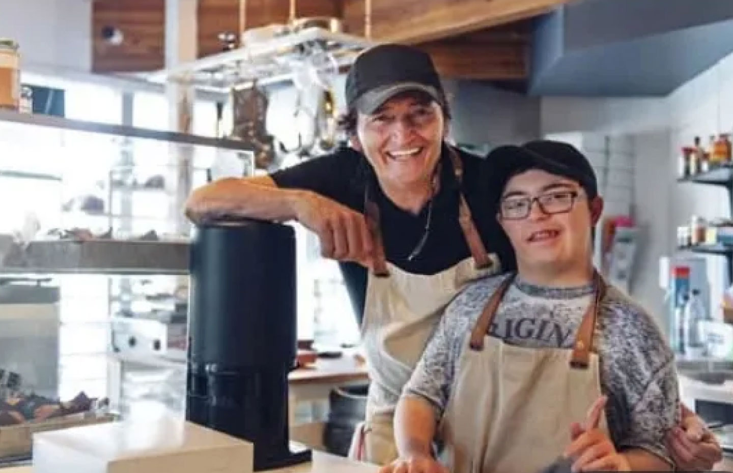 Man with disabilities at his job in the kitchen of a restaurant wearing an apron with, presumably, his boss