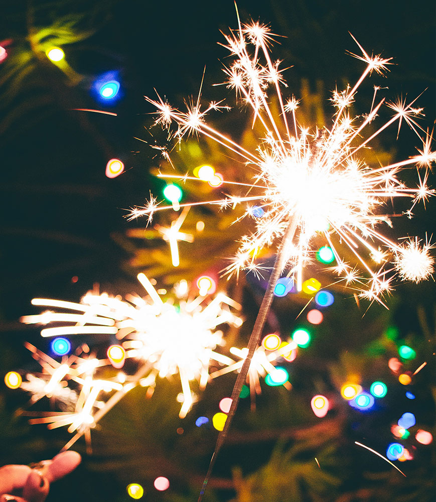 2 burning sparklers with multi-colored christmas lights in the background