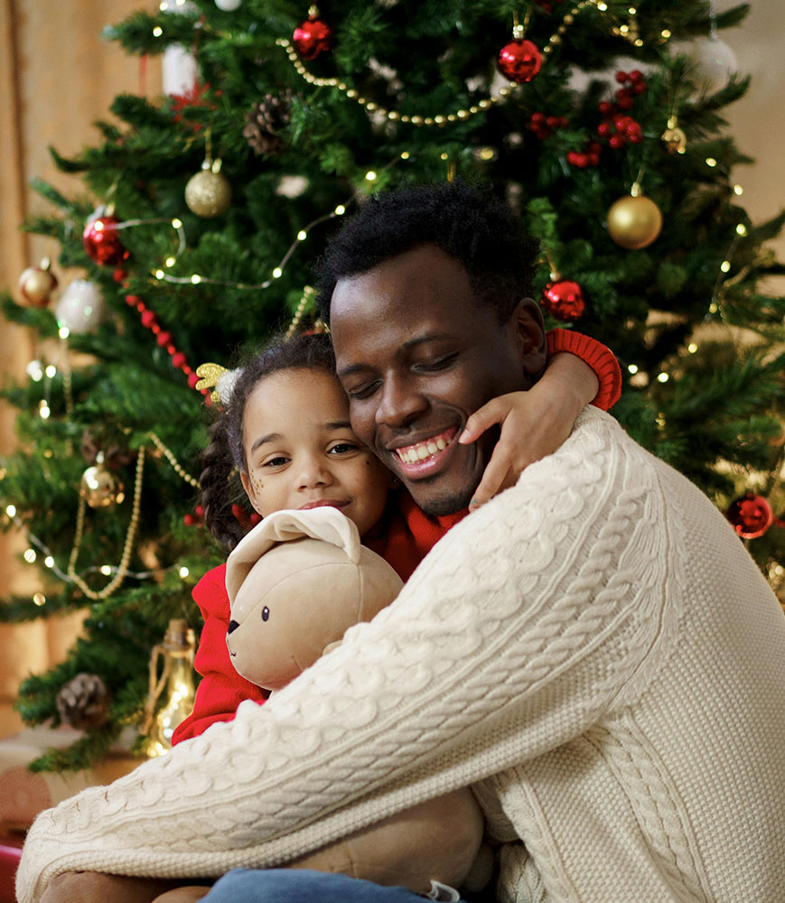 father & daughter hugging in front of their christmas tree